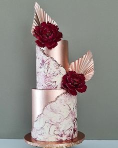 a three tiered cake decorated with pink and red flowers on a gold platter