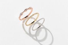 three different colored rings sitting on top of a white surface and one has a diamond in the middle