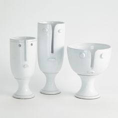 three white vases sitting next to each other on top of a table in front of a white background