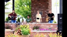 some people are playing music on the front porch with flowers and trees in the background