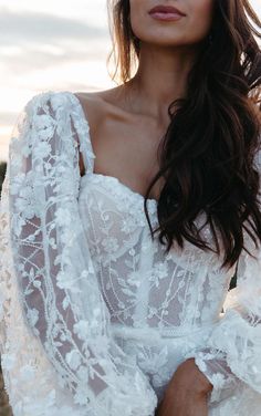 a woman wearing a white wedding dress with long sleeves and sheer lace on the shoulders