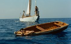 two people are in the water near a sailboat and one is laying on it