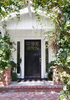 a black front door is surrounded by greenery and brick steps that lead up to the entrance