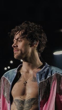 a man with tattoos on his chest wearing a pink and blue jacket in the dark