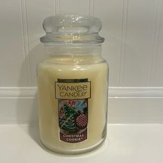 a yankee candle is sitting on a counter next to a white tile wall and a christmas ornament