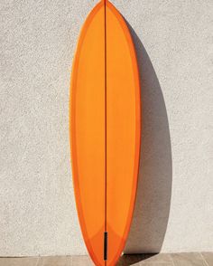 an orange surfboard leaning up against a wall