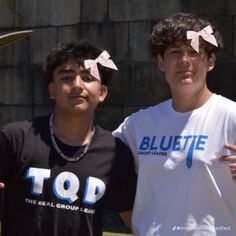 two young men standing next to each other in front of a building with pink bows on their hair