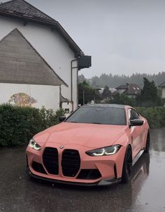 a pink sports car parked in front of a house on a rainy day with trees and bushes