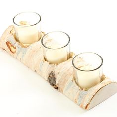 three candles sitting on top of a piece of wood with glass holders in the middle