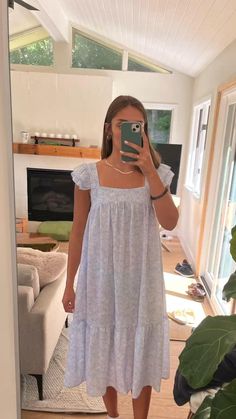 a woman taking a selfie in her living room while wearing a white dress and holding a cell phone