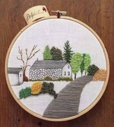 a cross stitch pattern with a house and road in the background on a wooden surface