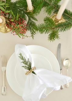 a place setting with white plates, silverware and greenery on the napkins