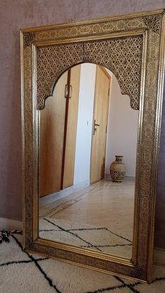 an ornate gold framed mirror on the floor in front of a wall with a vase