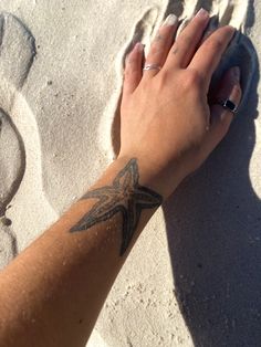 a woman's hand on the sand with a starfish tattooed on her arm