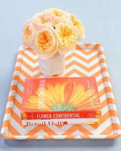 an orange and white chevroned tray with flowers on it, next to a book