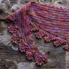 a crocheted shawl is laying on a piece of wood next to flowers