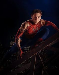 a man in a red and black spider suit on top of a metal structure with city lights behind him