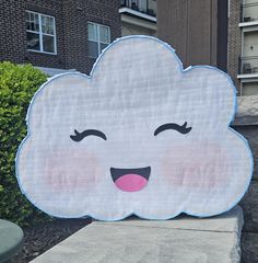 a large white cloud with pink cheeks and eyes sitting on top of a cement block