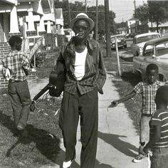 two men are standing on the sidewalk in front of some houses and one is holding an umbrella