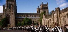 a group of people in graduation gowns walk down the street past an old building