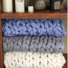 three blankets stacked on top of each other in front of a shelf filled with candles