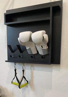 two white boxing gloves hanging on a black shelf with hooks and yellow leashes attached to it