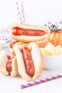 two hotdogs with ketchup, mustard and chips on a white table