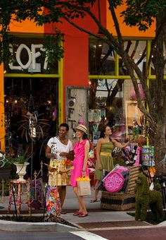 two women are standing in front of a store on the side of the street with their shopping bags