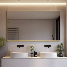 two white sinks sitting under a large mirror in a bathroom next to a potted plant