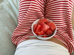 a bowl of watermelon sits on the back of a woman's stomach