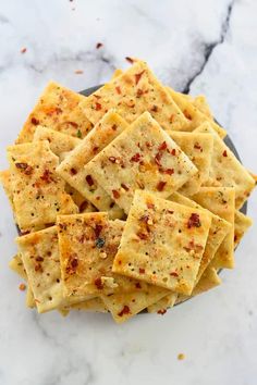 some crackers are on a black plate and white marble counter top with red chili sprinkles