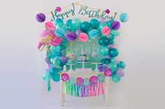 a birthday party with mermaid balloons and streamers on the wall, under a happy birthday sign