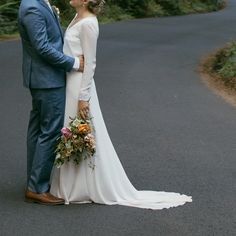 a bride and groom standing in the middle of a road with trees on both sides