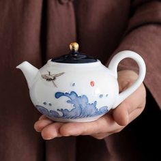 a person holding a tea pot with a dragon design on the front and side, in their hand