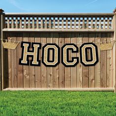 a wooden fence with the word hoco hanging from it's side in front of grass