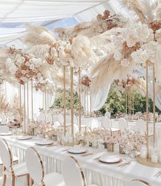 a long table with white chairs and tall centerpieces filled with flowers and feathers