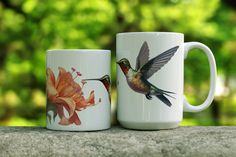 two coffee mugs with hummingbirds and flowers on them are sitting on a ledge