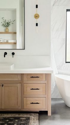 a white bath tub sitting next to a bathroom sink under a large mirror on top of a wooden cabinet