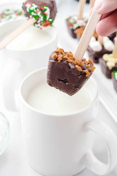 someone dipping some chocolate into a cup of milk with marshmallows and pretzels