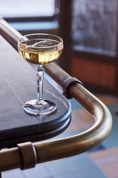 a glass filled with liquid sitting on top of a metal table next to a window