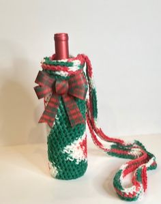 a crocheted wine bottle with a red and green ribbon tied around the neck