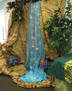 an indoor waterfall is decorated with blue and gold fabric, surrounded by potted plants