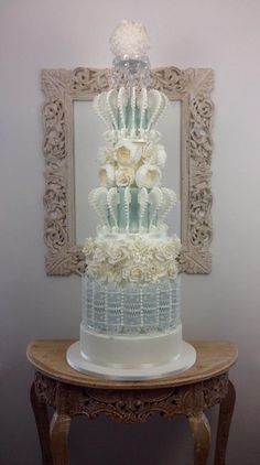 a wedding cake with white flowers on top is displayed in front of a framed mirror