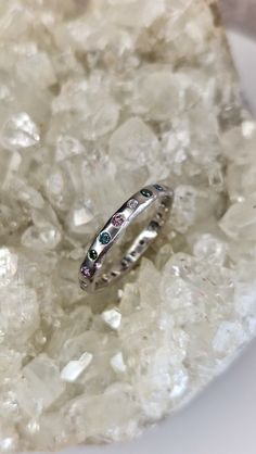 two wedding rings sitting on top of ice crystals in front of a white rock with green and blue stones