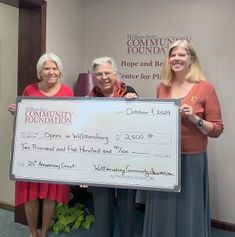 three women holding a large check for $ 1, 500 in front of a wall with the words community foundation written on it