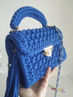 a hand holding a blue crocheted bag with a tasseled handle and chain