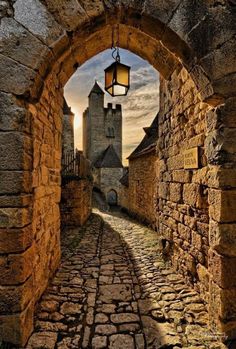 an old stone street with a light hanging from it's center and cobblestone walkway