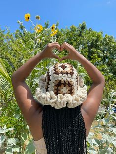 a woman wearing a crochet hat making a heart shape with her hands in the air