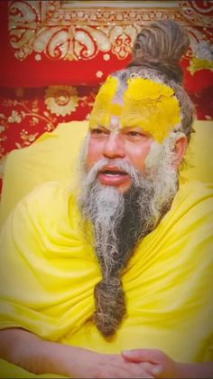 a man with yellow paint on his face and beard sitting in front of a red wall