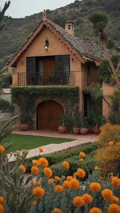 a house with orange flowers in front of it and a mountain behind the house that is surrounded by greenery